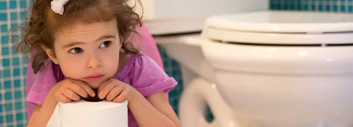 Een peuter in een paars T-shirtje zit naast een wc-pot terwijl ze een rol wc-papier vasthoudt.