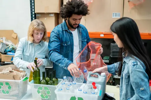 Drie mensen sorteren karton, glas en plastic in aparte containers.