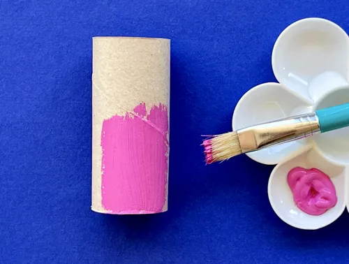 Deels roze geverfde wc-rol met een kunststof verfpalet met roze verf en een penseel ernaast.