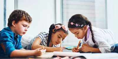 Drie kinderen tekenen met kleurrijk potlood terwijl ze op de vloer liggen