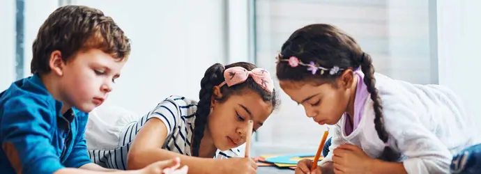 Drie kinderen tekenen met kleurrijk potlood terwijl ze op de vloer liggen