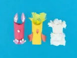 Een roze, gele en witte wc-rol waarop karton, propjes wc-papier en veertjes zijn geplakt om diertjes te maken.