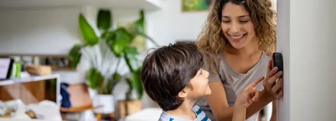 Een moeder met krullend haar en een lachende jongen verwisselen een thermostaat.