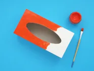 Een lege tissuedoos met verf en een kwast om een zelfgemaakt instrument van te maken.