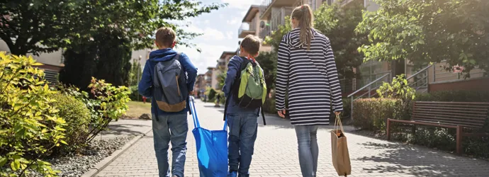 Vrouw en twee jongens met rugzakken lopen op straat en dragen herbruikbare booschappentassen.
