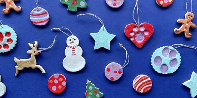 Diverse zoutdeeg kerstversieringen, zoals sneeuwpoppen, sterren, rendieren en kerstballen, op een blauwe achtergrond.