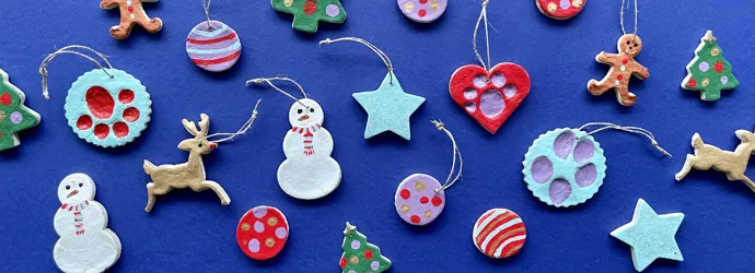 Diverse zoutdeeg kerstversieringen, zoals sneeuwpoppen, sterren, rendieren en kerstballen, op een blauwe achtergrond.