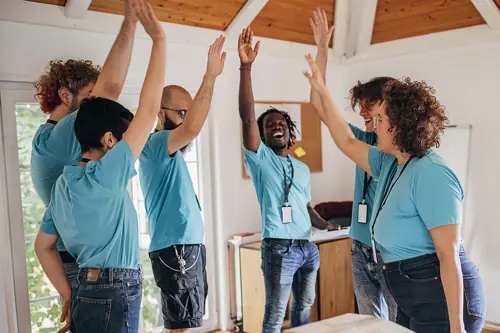 Zes mensen, allemaal in een blauw T-shirt, lachen en geven elkaar een high-five in een groep.