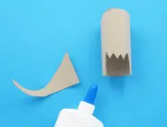 Uit wc-rol geknipte dinosauruskop en -staart met een lijmflesje.