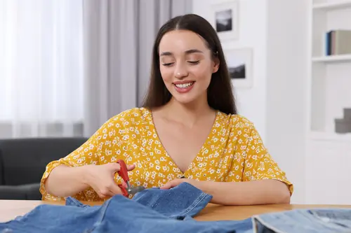 Een vrouw glimlacht terwijl ze met een schaar in een spijkerbroek knipt.