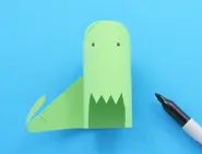 Groen geverfde dinosaurus van wc-rol met zwarte oogjes getekend met de zwarte viltstift die ernaast ligt.