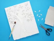 Blaadjes geknipt uit een lege tissuedoos worden geplakt op een tekening van een boom gevuld met repen keukenpapier.