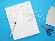 Blaadjes geknipt uit een lege tissuedoos worden geplakt op een tekening van een boom gevuld met repen keukenpapier.