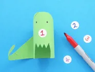 Groene dinosaurus van wc-rol met nummer 1 op een wit rondje papier; nummers 2, 3 en 4 en een rode stift liggen ernaast.