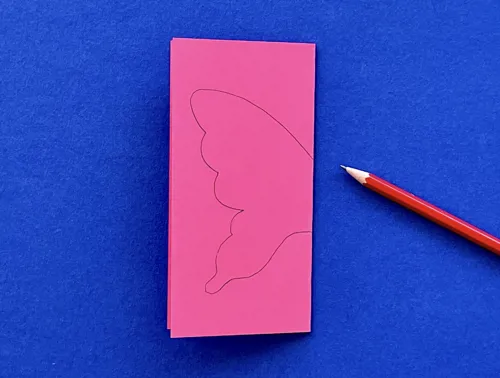 Dubbelgevouwen roze karton waarop een vlindervleugel is getekend met een potlood ernaast.