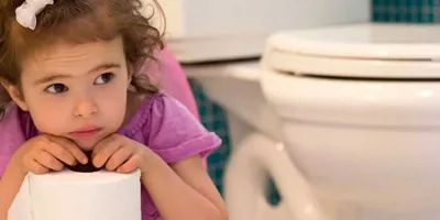 Een peuter in een paars T-shirtje zit naast een wc-pot terwijl ze een rol wc-papier vasthoudt.