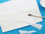 Repen gescheurd keukenpapier zijn op een vel tekenpapier geplakt met de kwast die er bovenop ligt.