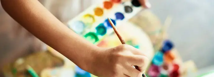 Een kind houdt een palet vat en gebruikt een kwast op een doek