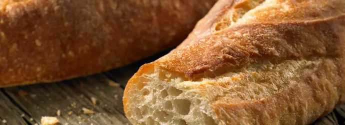 Close-up van een doorgesneden knapperig wit stokbrood met kruimels en een tweede stokbrood in de achtergrond