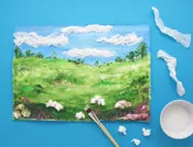Een landschap geschilderd op met keukenpapier beplakt papier met wolken van propjes papier en restjes papier ernaast.