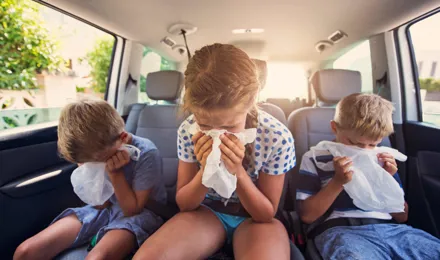 Drie kinderen zitten op de achterbank van een auto over plastic zakjes gebogen alsof ze moeten overgeven.