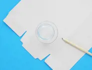 Een plat geopende tissuedoos wordt op een blauw oppervlak gelegd met een lege beker en een potlood.