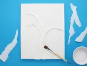 Repen gescheurd en gepropt keukenpapier worden op een potloodtekening van een boom geplakt met lijm en een penseel.