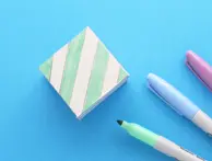 Een kartonnen kubus met mintgroene diagonale strepen en drie viltstiften ernaast.