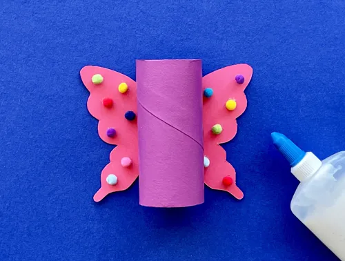 Een roze wc-rolkoker wordt op een met gekleurde bolletjes versierde kartonnen vlinder geplakt.