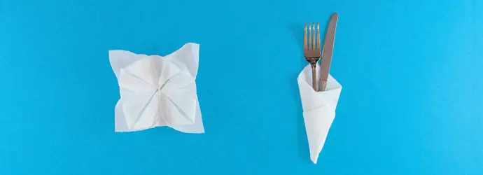 Decoratief gevouwen servetten in een bloemvorm en een kegel rond een mes en vork