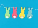 Garen is geregen door de oren van vier gekleurde kartonnen konijntjes om een paasslinger te vormen.