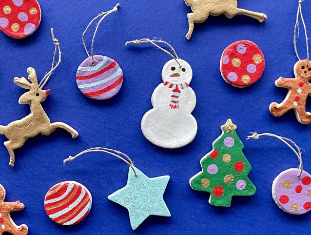 Kerstversiering van zoutdeeg, zoals een sneeuwpop, kerstboom, ster, rendier en kerstballen, op een blauwe achtergrond.