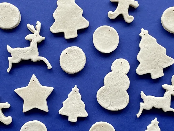 Zoutdeeg figuurtjes in de vorm van rendieren, sneeuwpoppen, kerstbomen en rondjes op een blauwe achtergrond.