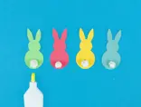 Vier kartonnen konijntjes in groen, roze, geel en blauw waarop propjes wc-papier zijn geplakt als staartjes.