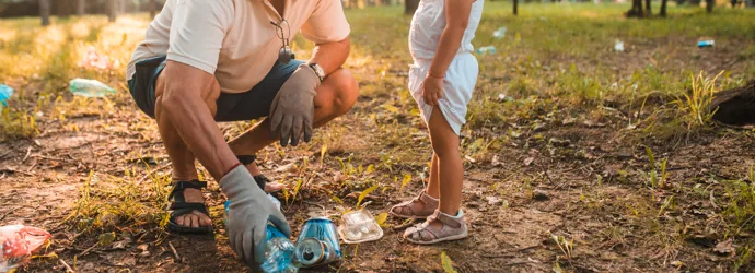 Opa leert peuter zwerfvuil te verzamelen in een zonovergoten park.